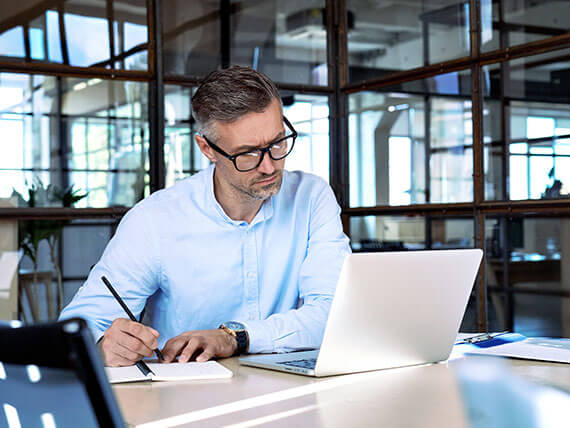 Male business executive looking at laptop computer and taking notes in an office